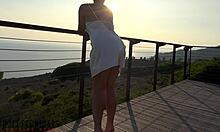 Piersiasta dojrzała kobieta w białym satynowym stroju angażuje się w aktywność seksualną na balkonie na zewnątrz podczas zachodu słońca